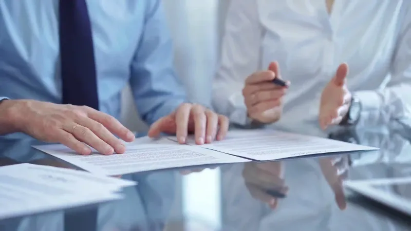 Manos de profesionales analizando documentos contractuales sobre escritorio brillante