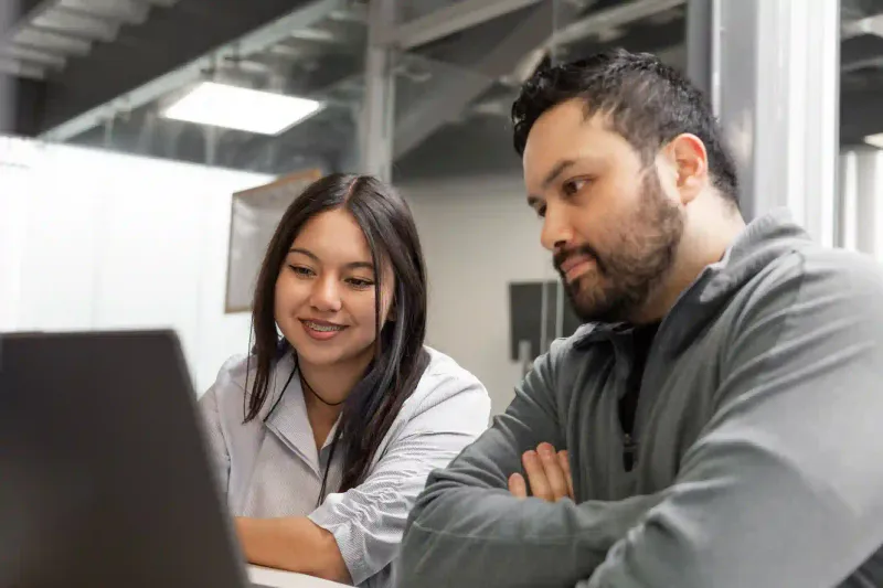 Profesional joven y cliente con barba revisan información en laptop durante consulta en oficina moderna