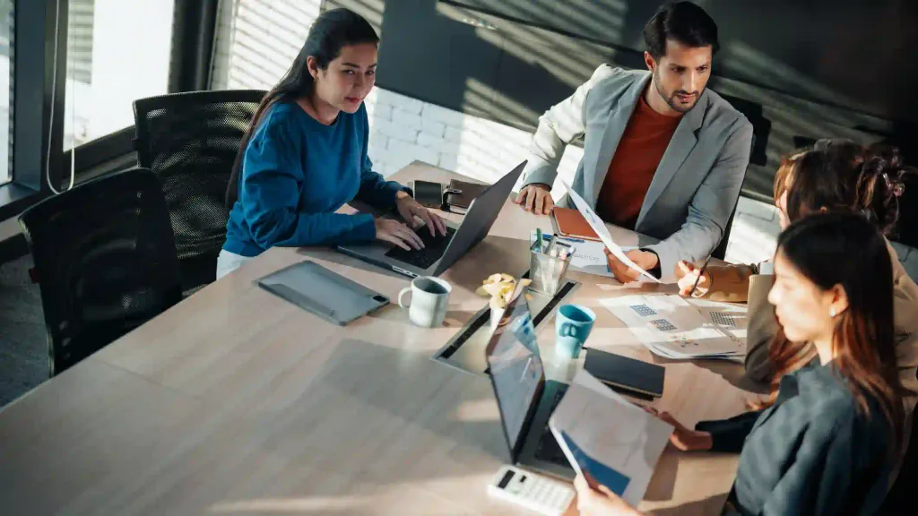 Equipo de cuatro profesionales analiza documentos y laptops sobre mesa de reunión en oficina moderna