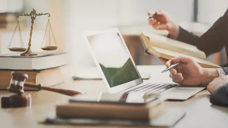 Abogados revisan libros de derecho y laptop sobre escritorio con balanza y martillo de juez