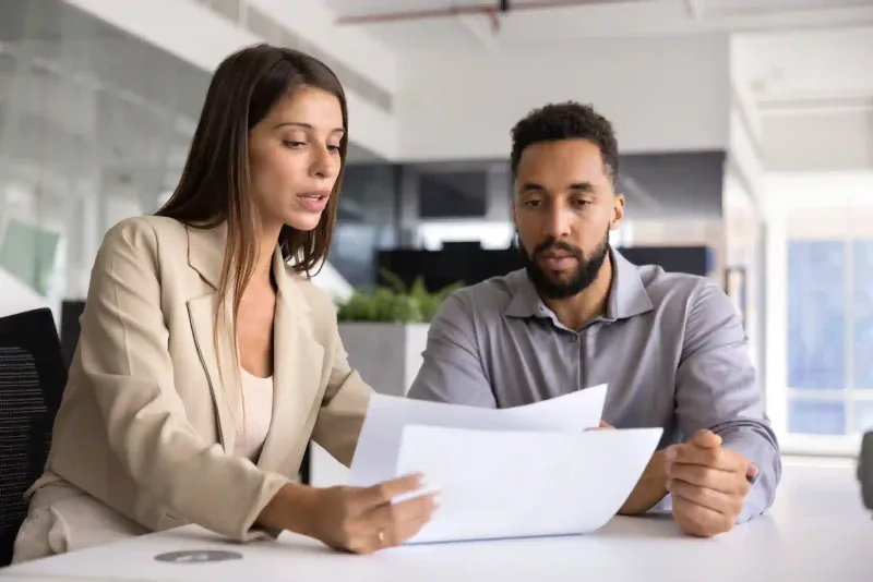Asesora explica documento a cliente con barba durante reunión profesional en oficina moderna