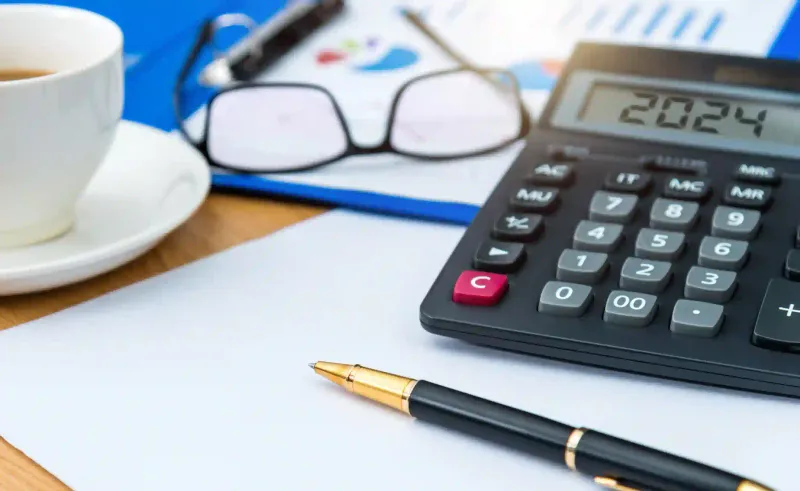 Calculadora, lapicera, anteojos sobre carpeta con gráficos financieros y taza de café en escritorio de planificación