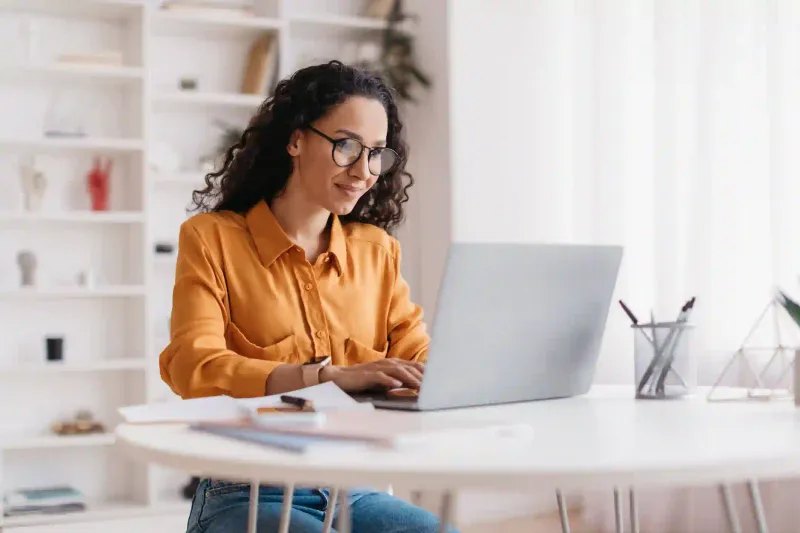 Emprendedora con anteojos trabajando en laptop para gestionar trámite empresarial