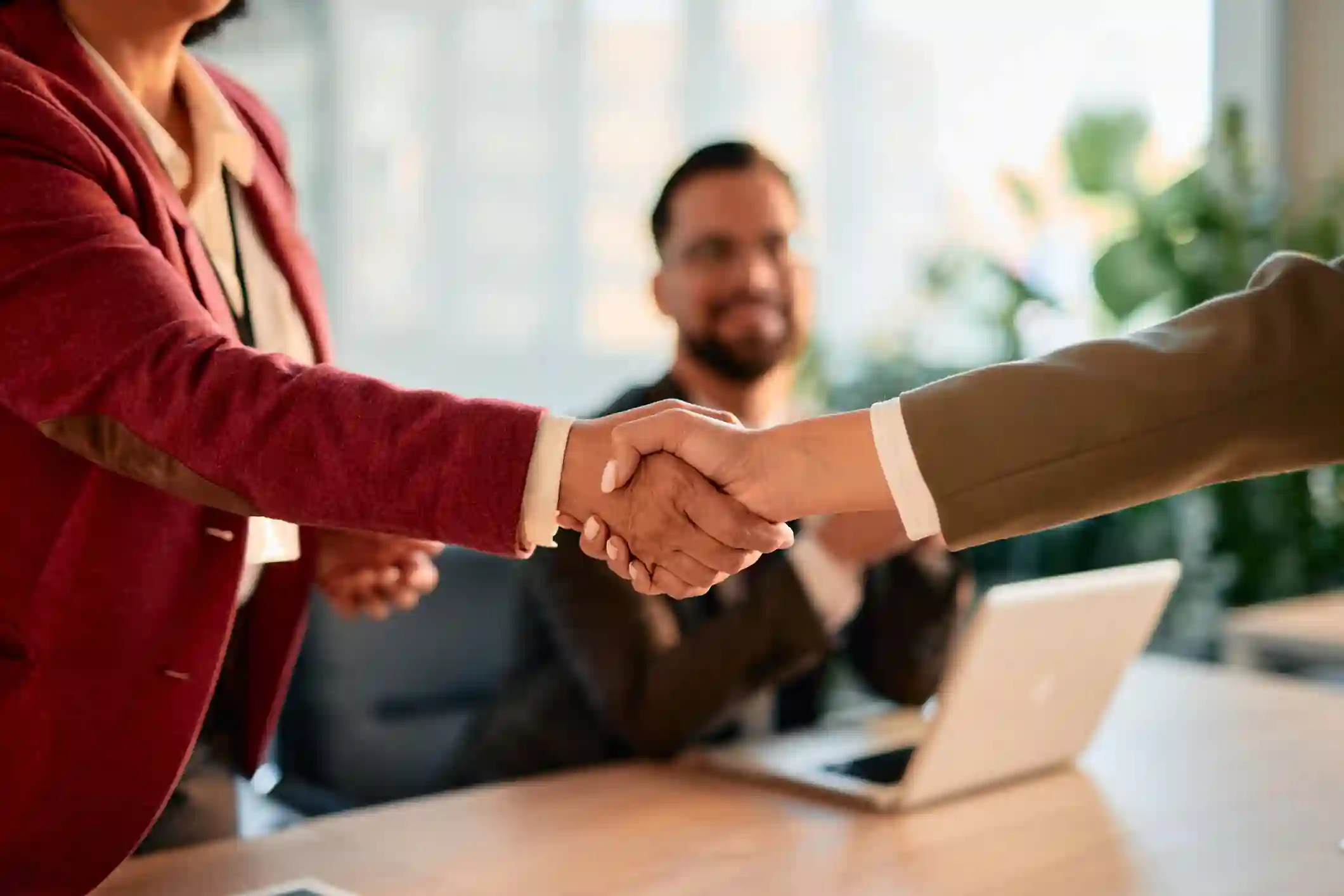 Apretón de manos entre dos profesionales tras reunión de negocios con observador
