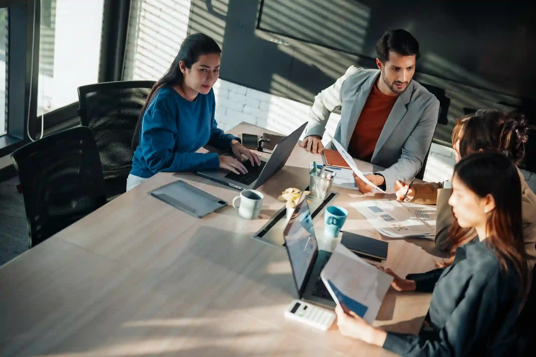 Equipo de cuatro profesionales analiza documentos y laptops sobre mesa de reunión en oficina moderna