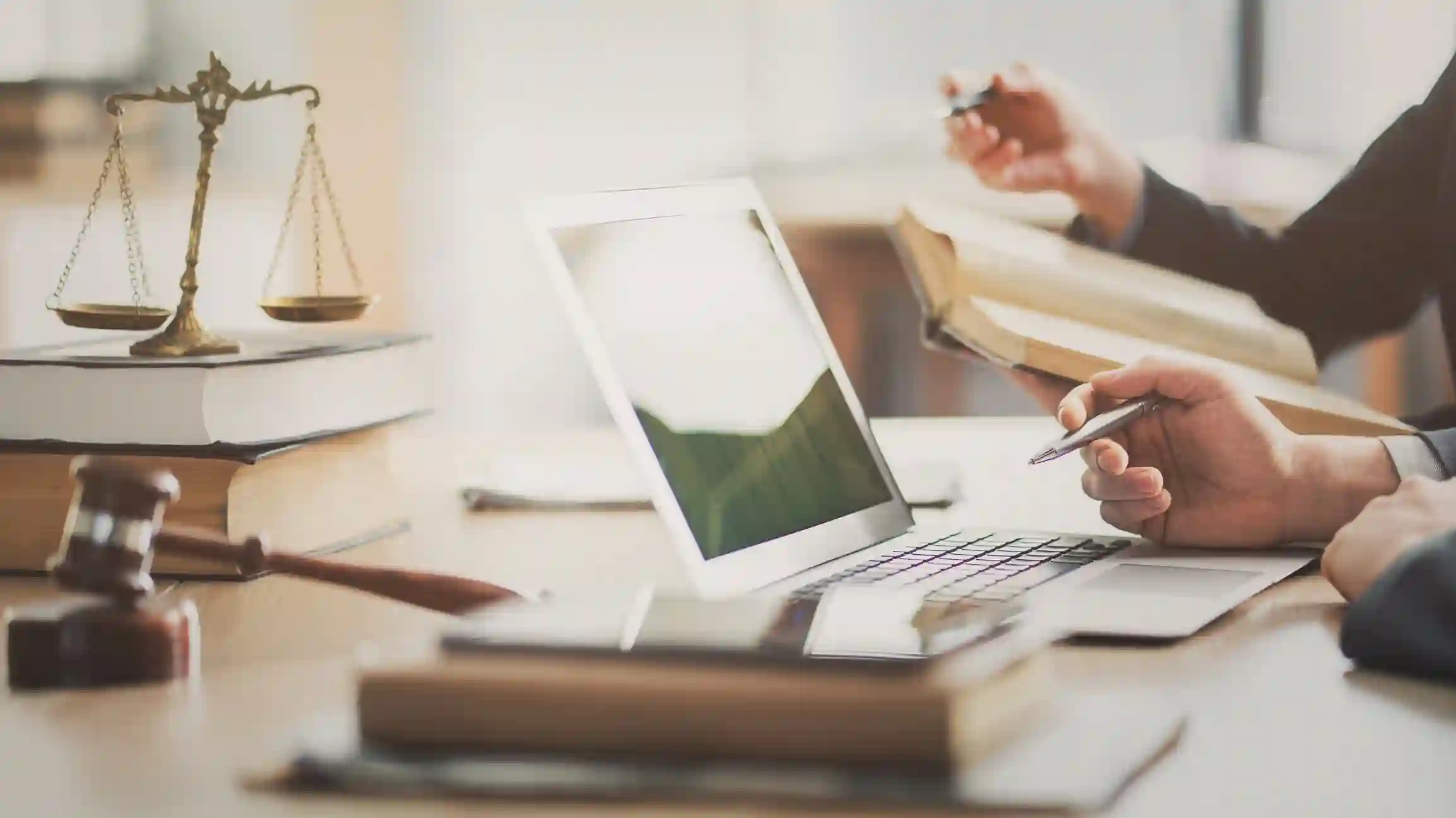 Abogados revisan libros de derecho y laptop sobre escritorio con balanza y martillo de juez
