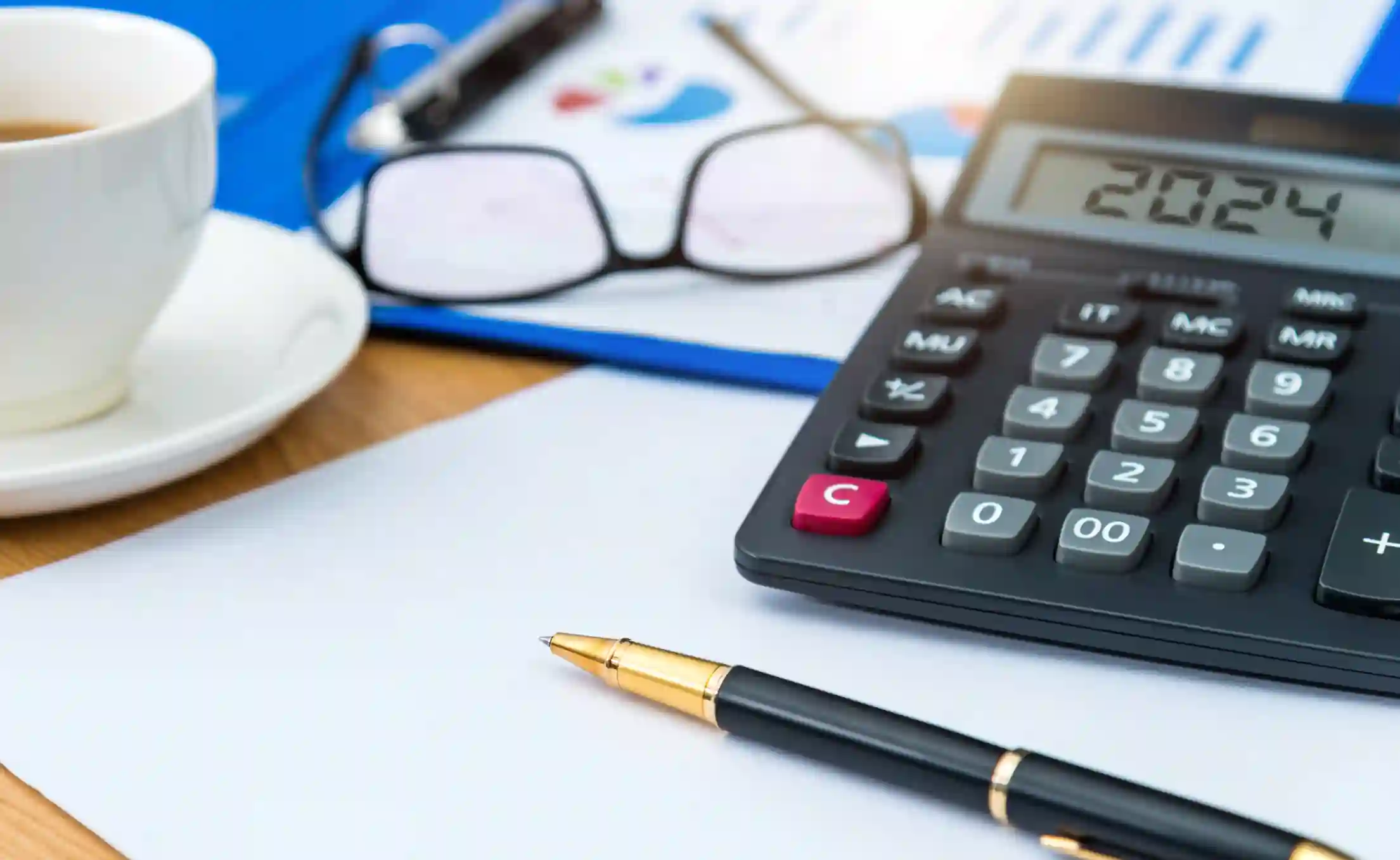 Calculadora, lapicera, anteojos sobre carpeta con gráficos financieros y taza de café en escritorio de planificación