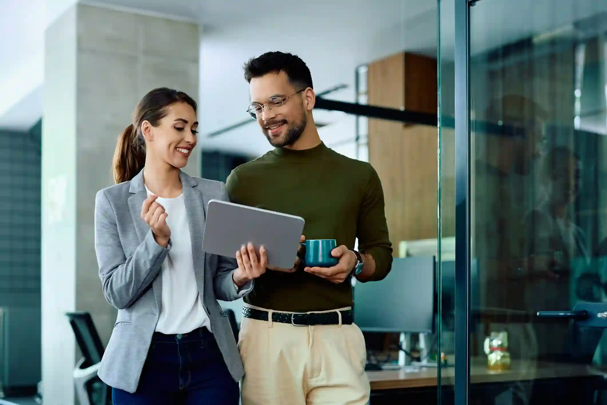 proteccion-datos-personales-ecuador-asesoria-empresa Pareja de profesionales sonríe mientras revisa información en tablet en oficina moderna con paredes de vidrio