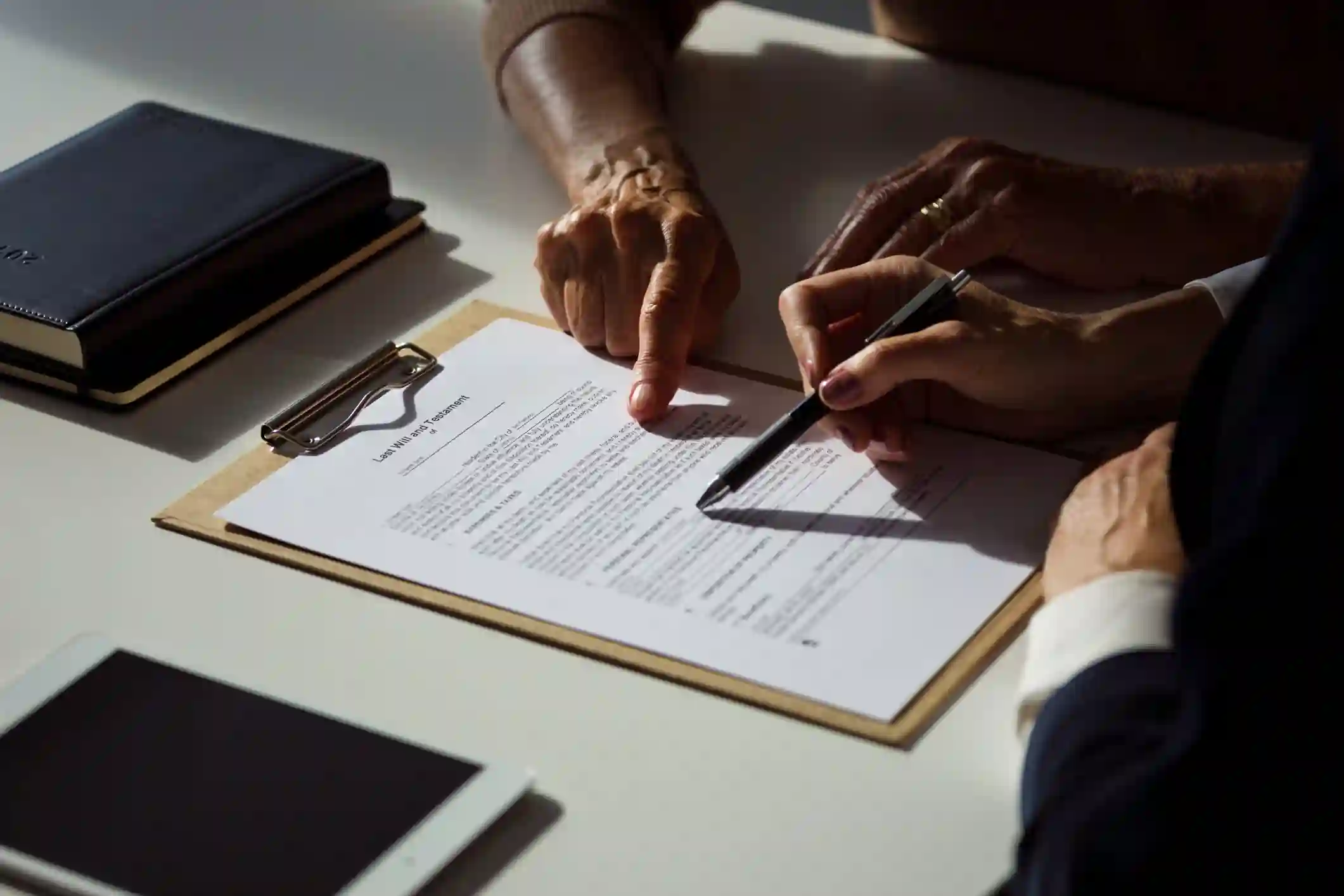 Dos personas revisan documento legal en clipboard sobre escritorio claro con cuaderno y tablet