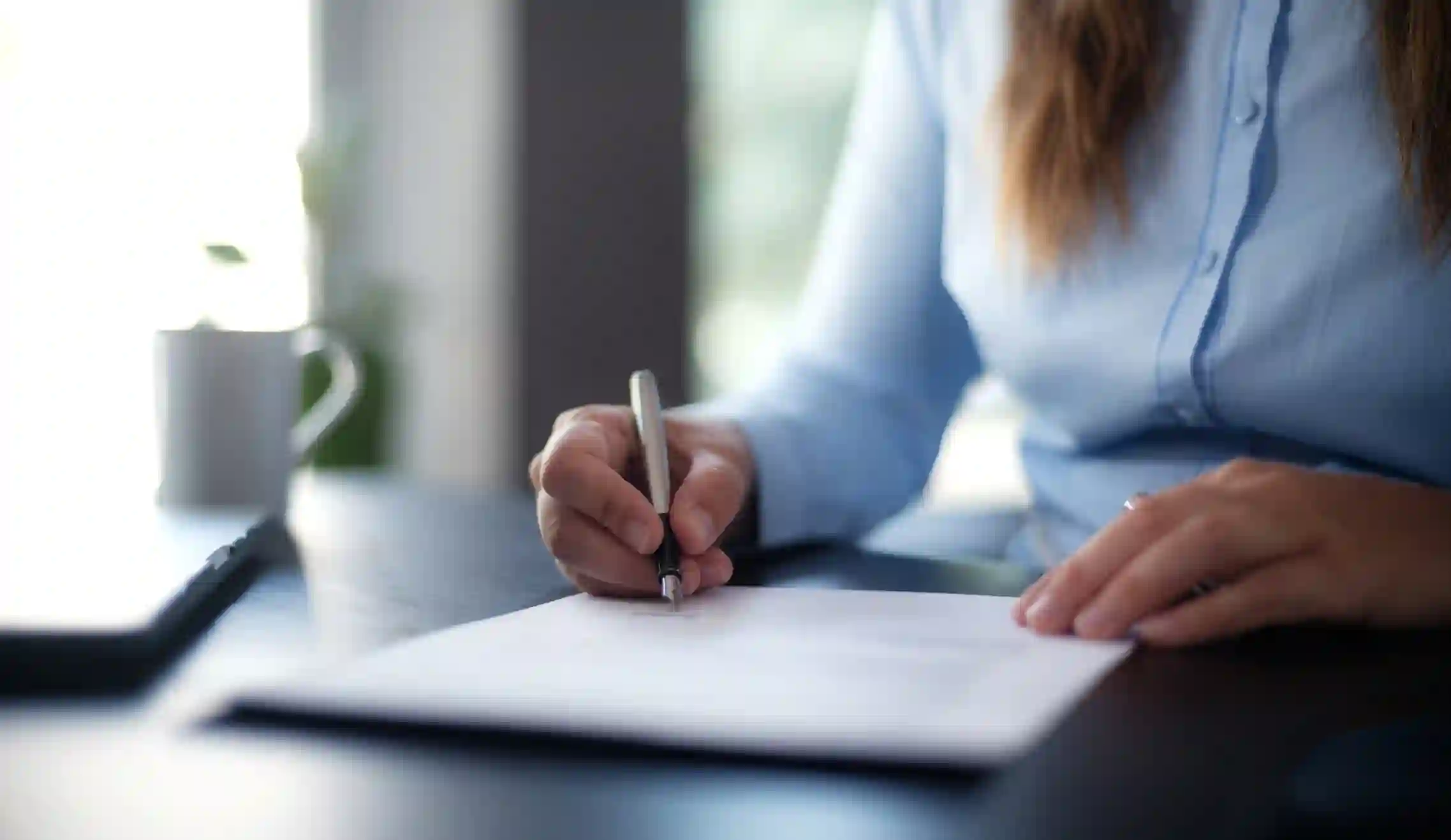 Persona firma documento formal con lapicera sobre escritorio oscuro con luz natural
