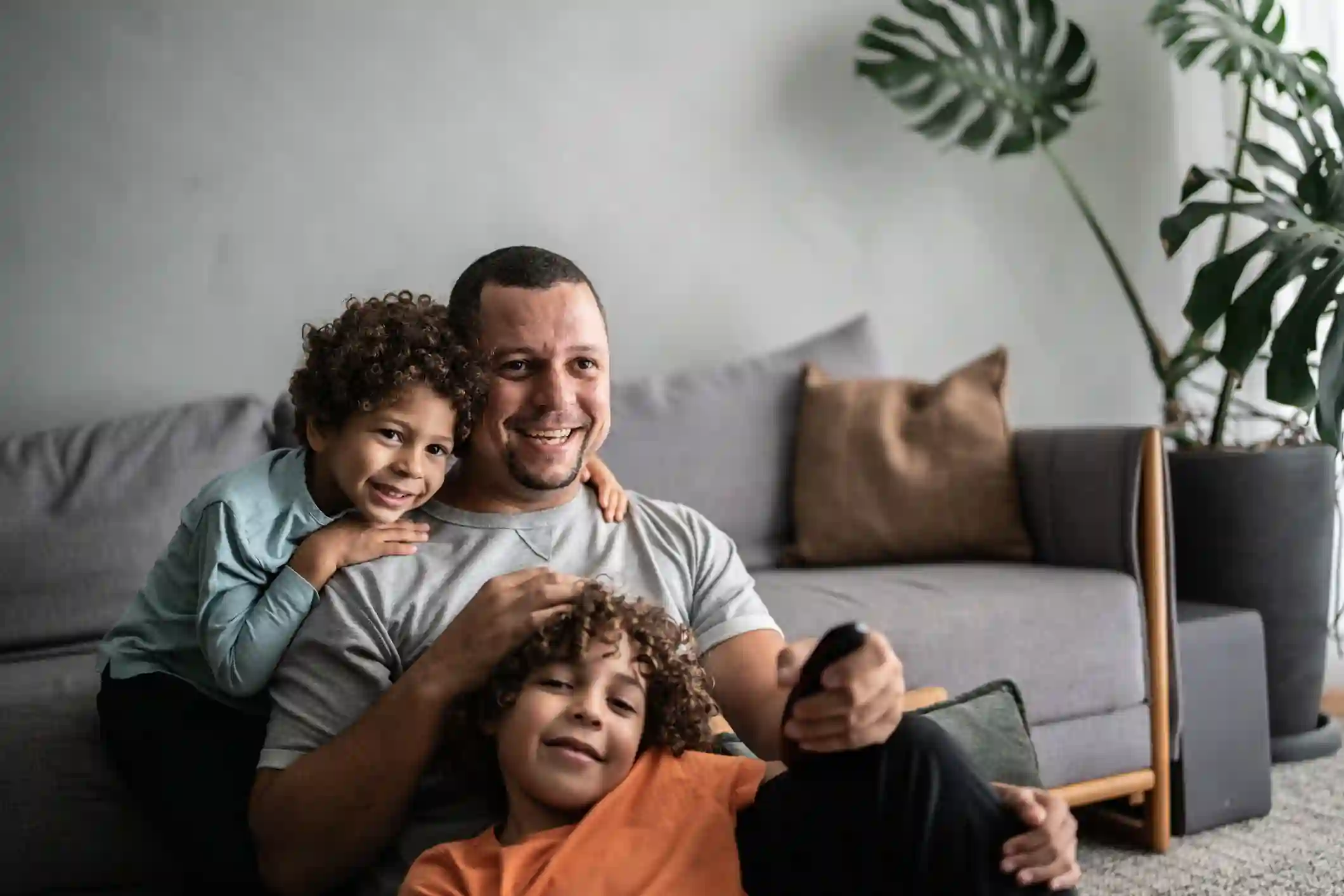 Padre con dos hijos pequeños comparten momento cotidiano en sala del hogar con planta