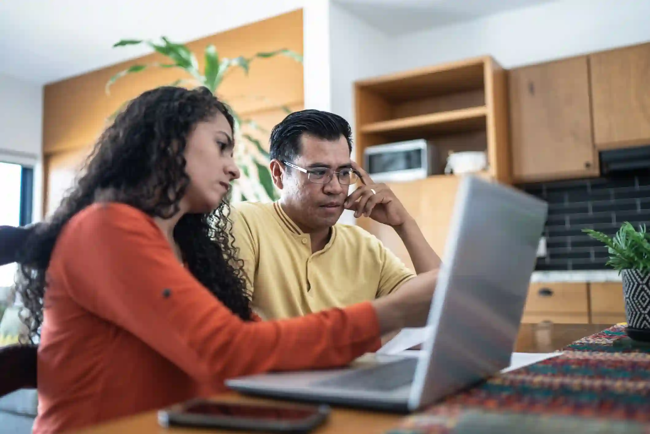 Pareja revisa sus cuentas y facturas frente al laptop en la cocina de casa